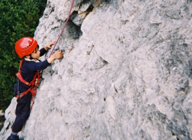 nino con casco rojo escalando por una montana